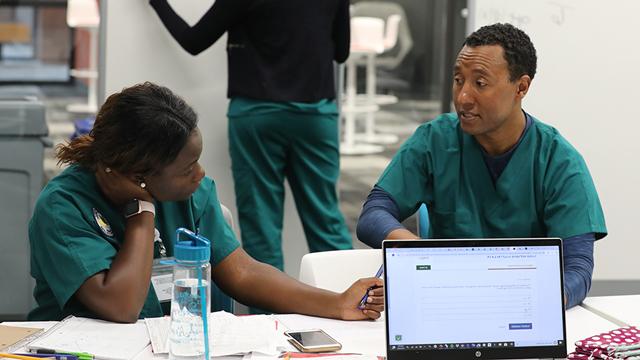 2 medical students sit at a table and work on an assignment