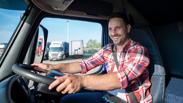 A man smiles from behind the steering wheel of a semi truck