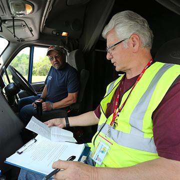 一名CDL讲师坐在一辆商用卡车的驾驶室里，与一名学生司机一起检查清单.