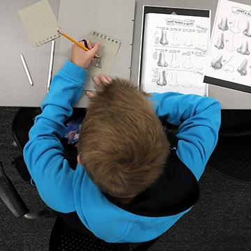 一个男孩坐在书桌前画人的鼻子