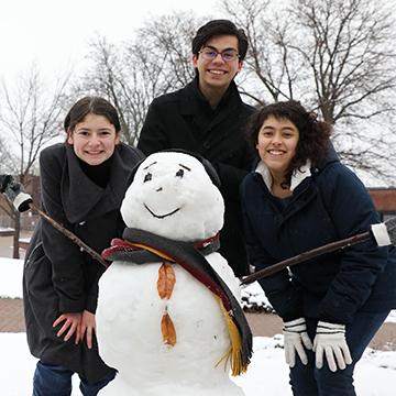 Three honors students posing by a snowman the built during the winter