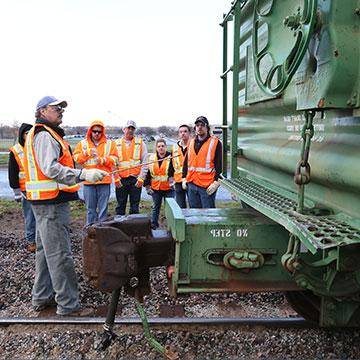 An instructor points out items on a rail car to a group of students.