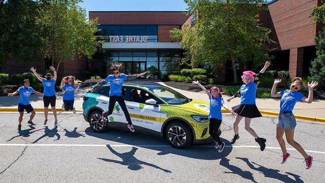 Driver's education students jumping for joy in front of an electric car