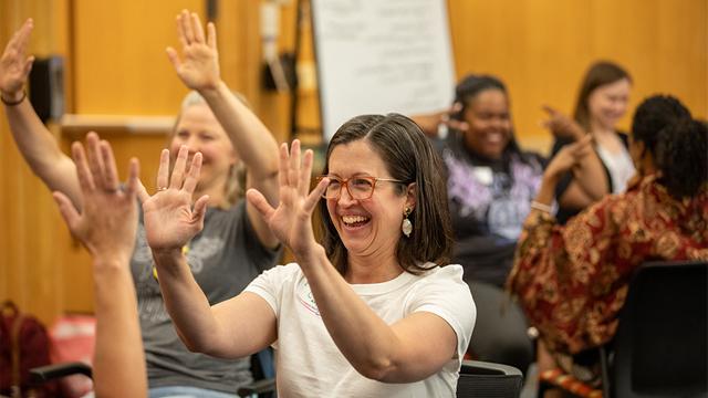 teachers in a workshop smiling and  gesturing with their hands raised