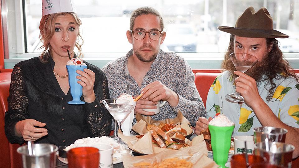 three people sitting in a diner booth drinking and eating